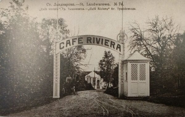 Senas atvirukas su arka „Cafe Riviera“ prie kelio, sargo būdelė, medžiai, žmonės tolumoje