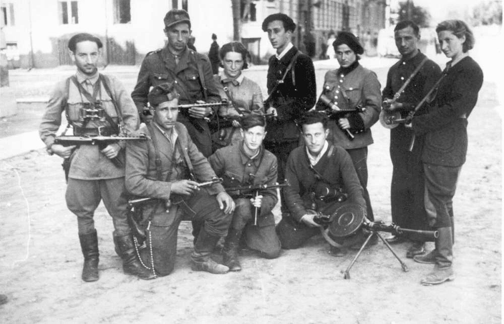 Vienuolika ginkluotų partizanų su automatais ir kulkosvaidžiu pozuoja miestelio aikštėje, nespalvota nuotrauka
