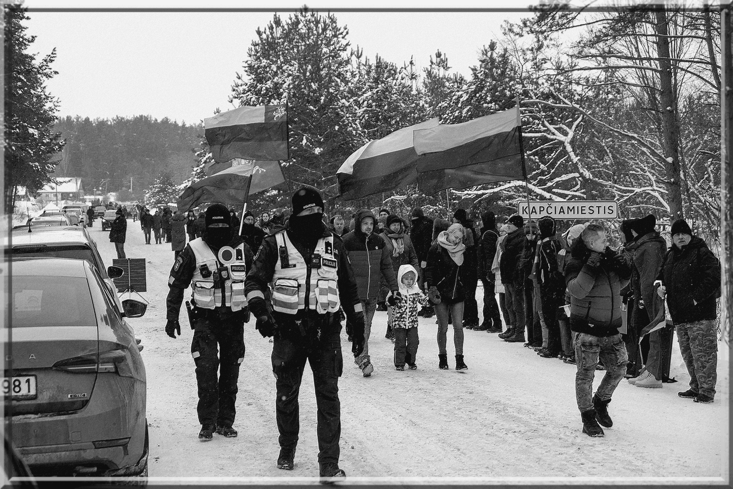 Policininkai eina sniegu užklotu keliu prieš protestuotojų grupę su vėliavomis prie Kapčiamiesčio ženklo